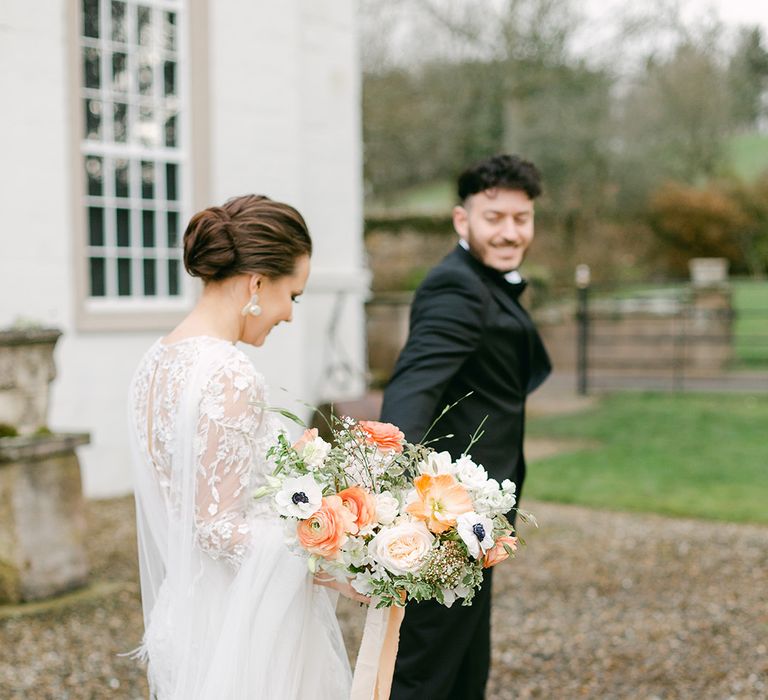 Bride in an applique wedding dress with rings wearing bow wedding shoes and holding a peach and white wedding bouquet 