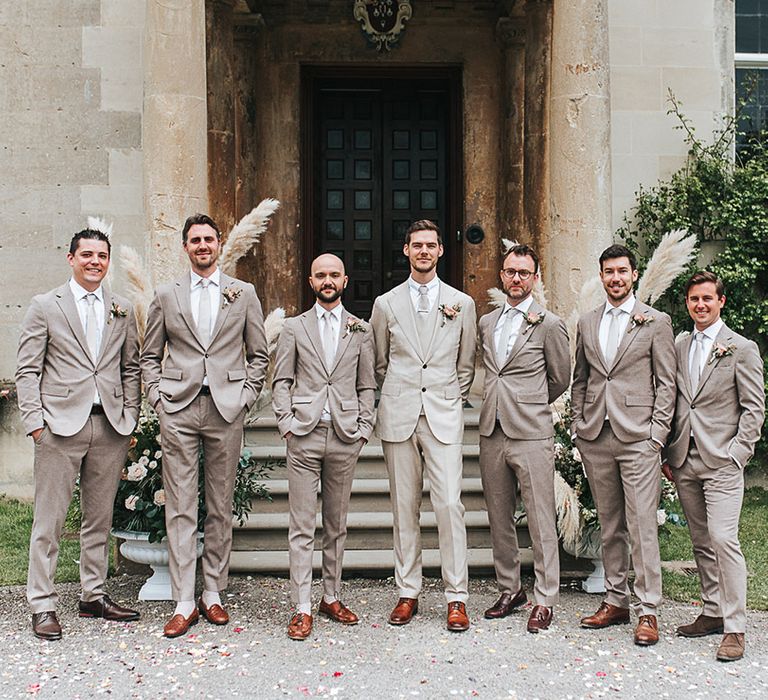 Groom stands with his groomsmen for the wedding day all in matching neutral wedding suits 