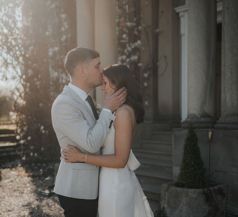 Bride and groom hug as the groom kisses the bride on her forehead 