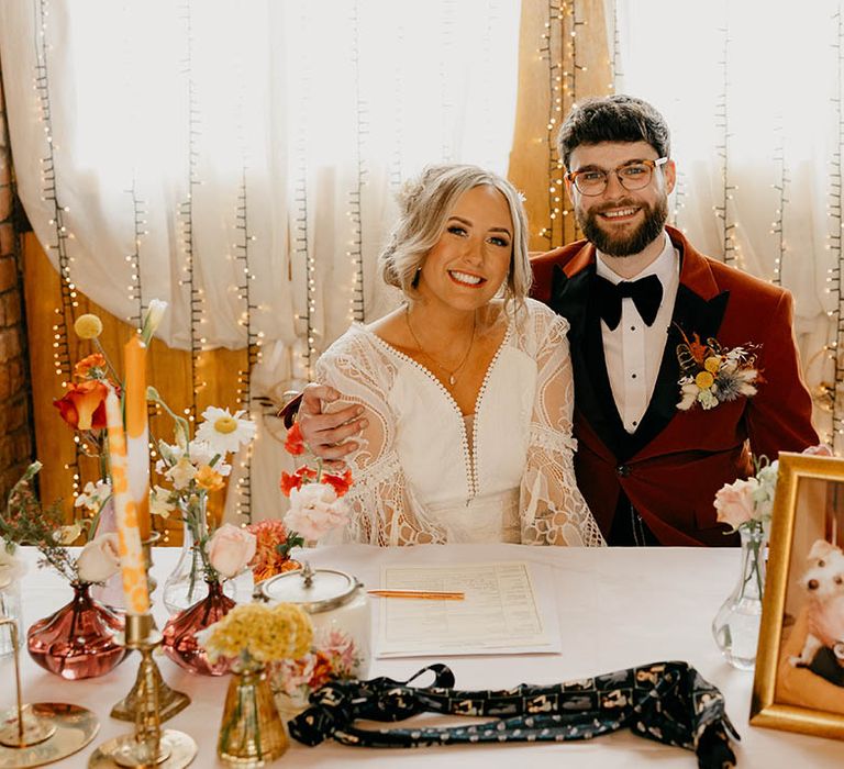 Bride and groom sign their register with orange and yellow wedding flowers for their retro theme wedding 