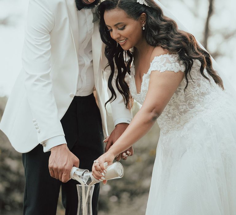 Bride & groom place sand inside glass during wedding ceremony outdoors in Phuket 