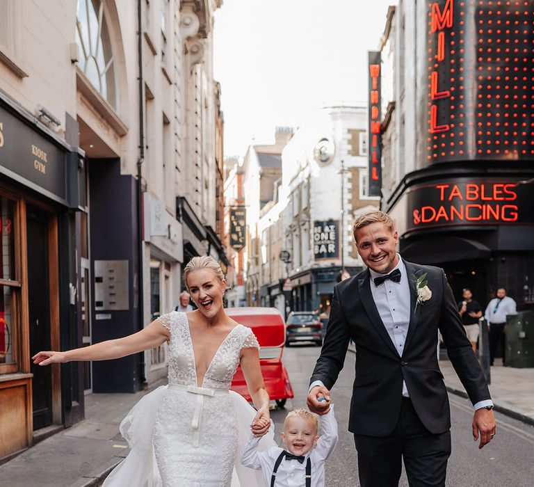 Bride & groom walk with their son through the city of London on their wedding day 