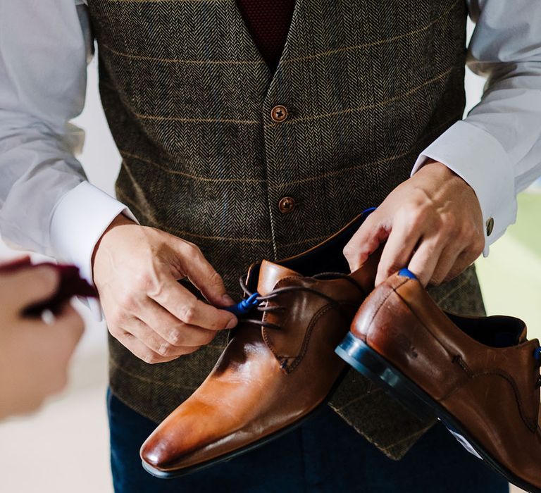 Groom wearing tartan waistcoat holds brown brogue wedding shoes 