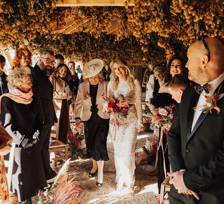 Mother of the bride walks the bride down the aisle in a high neck long sleeve lace wedding dress 