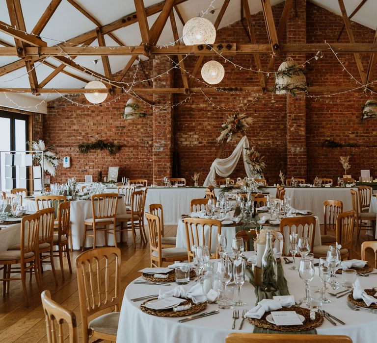 Earthy and neutral reception room at The Green Cornwall with minimalist white tablescape design, fairy lights, dried flower arrangements, and a large wooden triangular arch