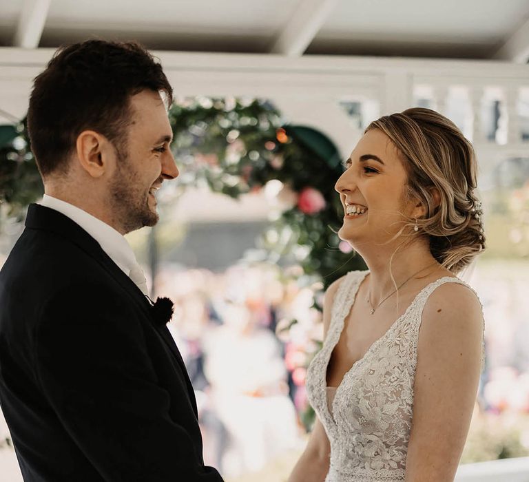 Bride in a lace wedding dress and groom in black three piece suit holding hands for their outdoor wedding ceremony 