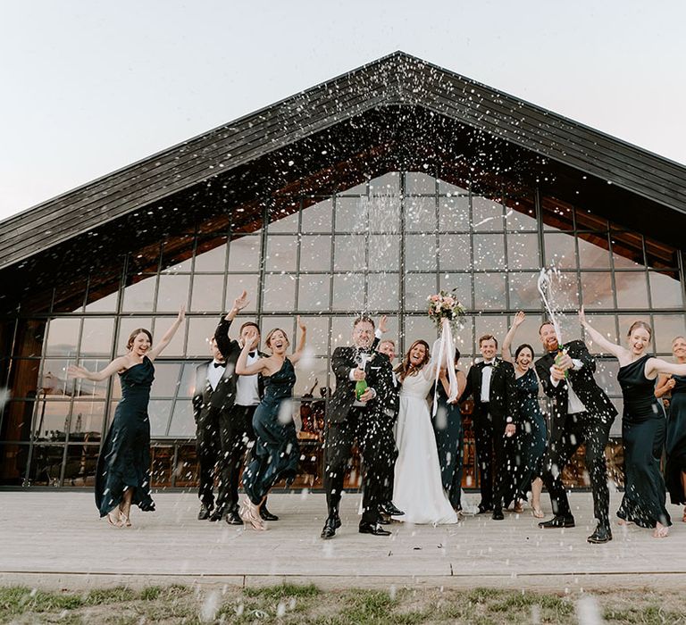 Bride & groom stand with wedding party outdoors during champagne spray picture