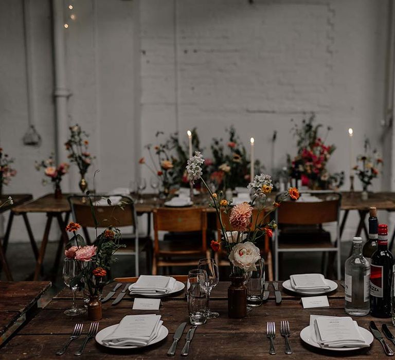 Neutral minimalist Hackney Studios wedding tablescape with tall tapered white dinner candles and pops of colour in floral and foliage decorations