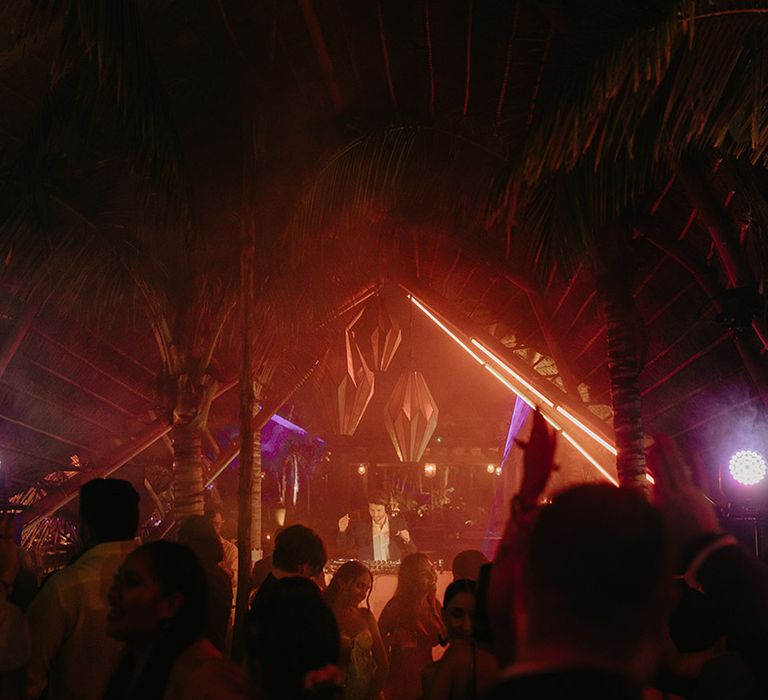 Wedding guests gather around DJ booth outdoors during rave wedding reception in the jungle 