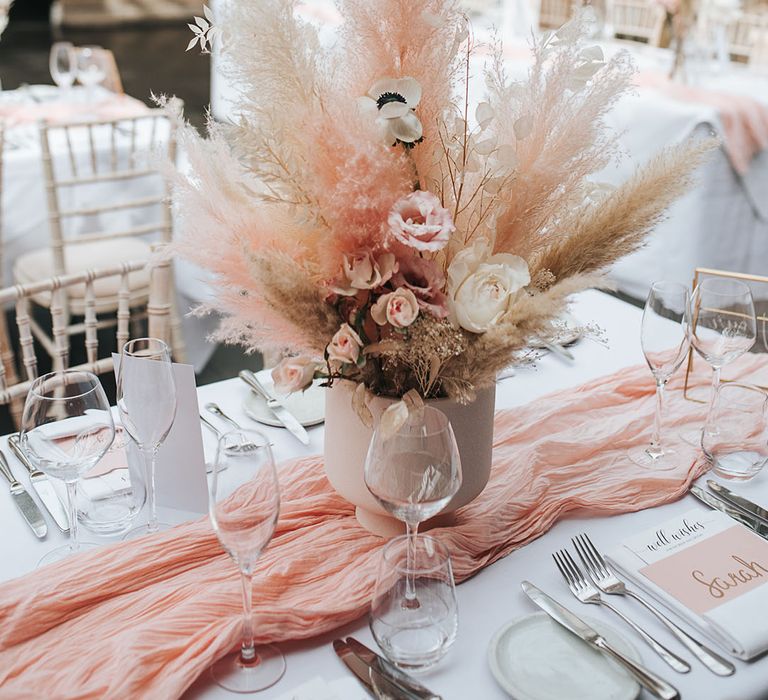 Pink and white pampas grass centrepiece decor with white poppies and roses in a white vase on the table with a pink table runner 