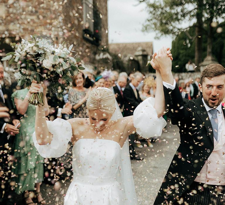 Bride in Jesus Peiro puffed sleeve wedding dress celebrates as she walks through colourful confetti exit with her groom