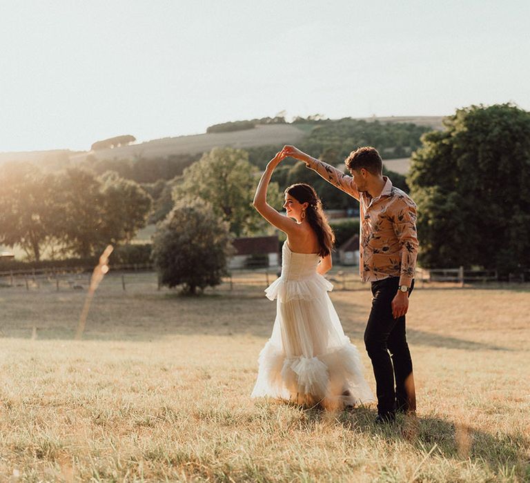 Bride in strapless ruffle wedding dress being spun by the groom in a Hawaiian style summer pink shirt during golden hour 