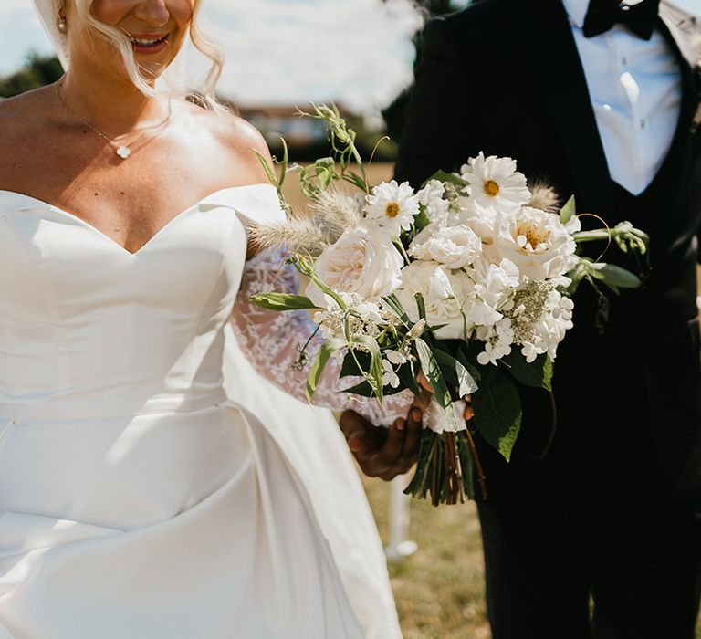 Bride carries classic white floral bouquet complete with green foliage 