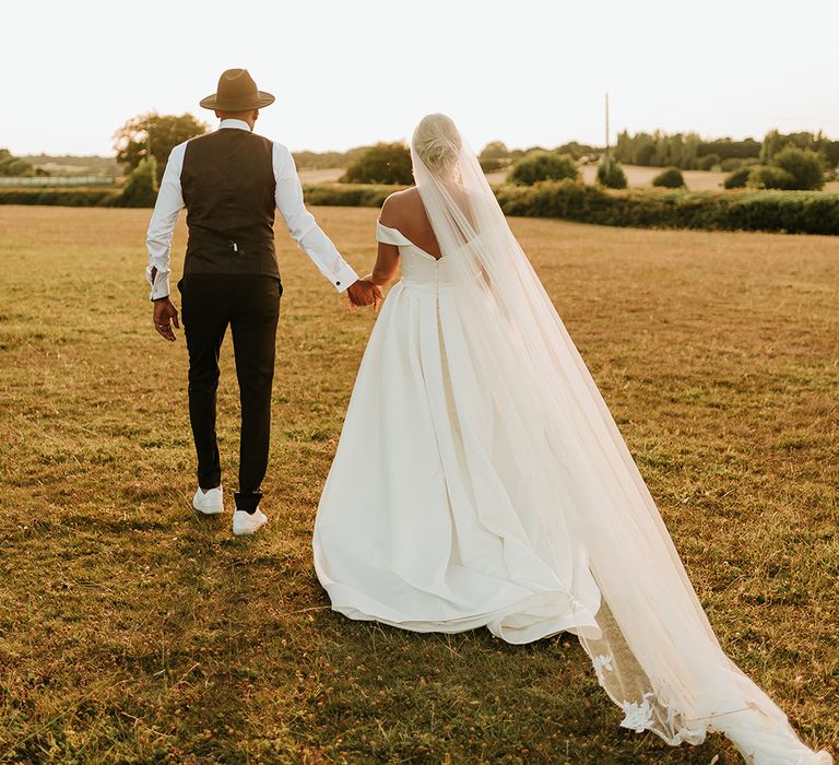 Bride in drop veil walks alongside her groom during golden hour portraits 