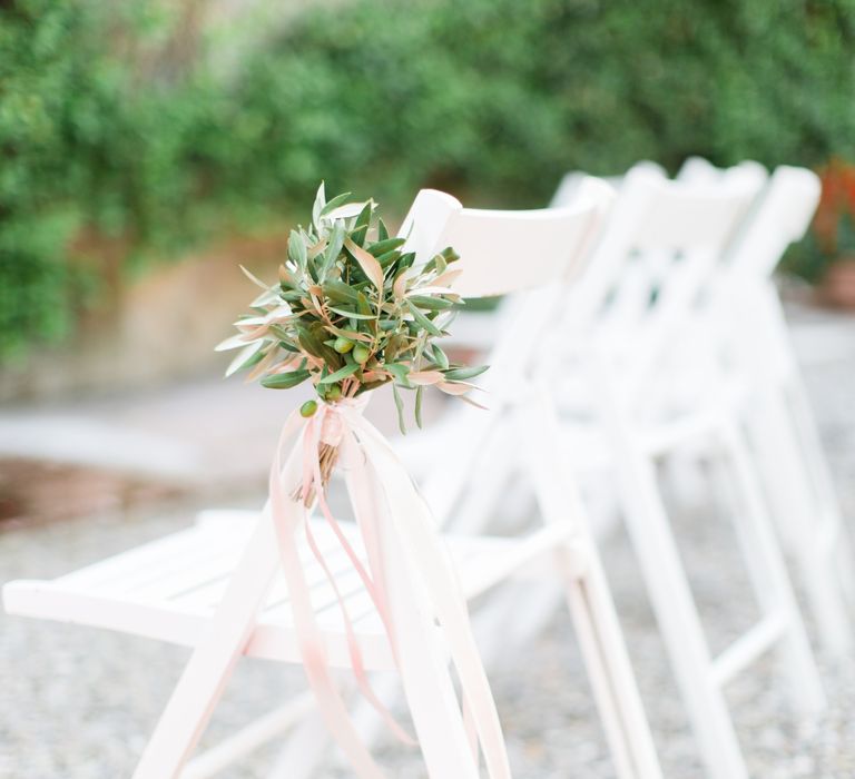 Bright white wedding chairs with decorated with foliage tied with pale pink ribbon 