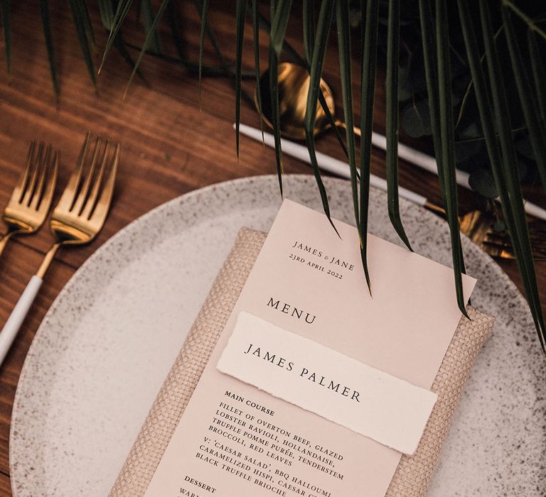 Speckled wedding plate with beige wedding menu with napkin and white and gold cutlery with leaf table arrangements 