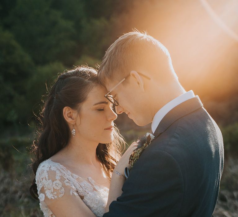 The bride and groom rest their foreheads against each other for golden hour portraits on their wedding day 