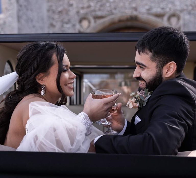 Bride and groom sharing glass of pink champagne in the back of classic vintage wedding car 