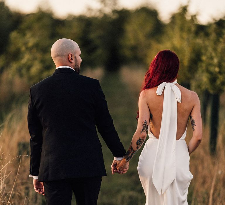 Bride in low back Halfpenny London wedding dress with black wedding shoes by Manolo Blahnik walking holding hands with the groom 