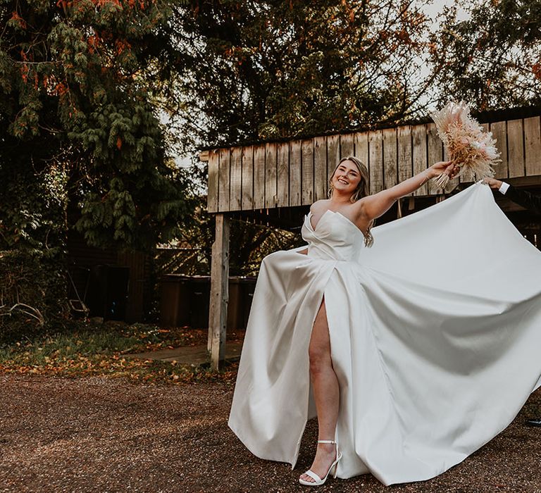 Groom in black velvet tuxedo holds the gigantic wedding skirt from the bride's strapless wedding dress with high leg slit 