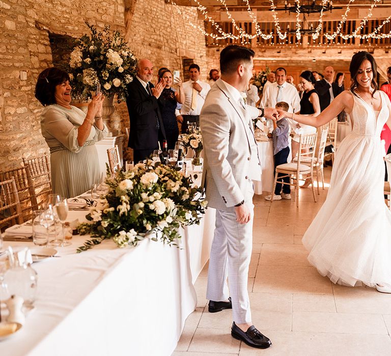 groom in al light blue suit twilling his bride in a princess wedding dress at their Caswell House rustic luxe wedding reception with fairy lights draped from the ceiling