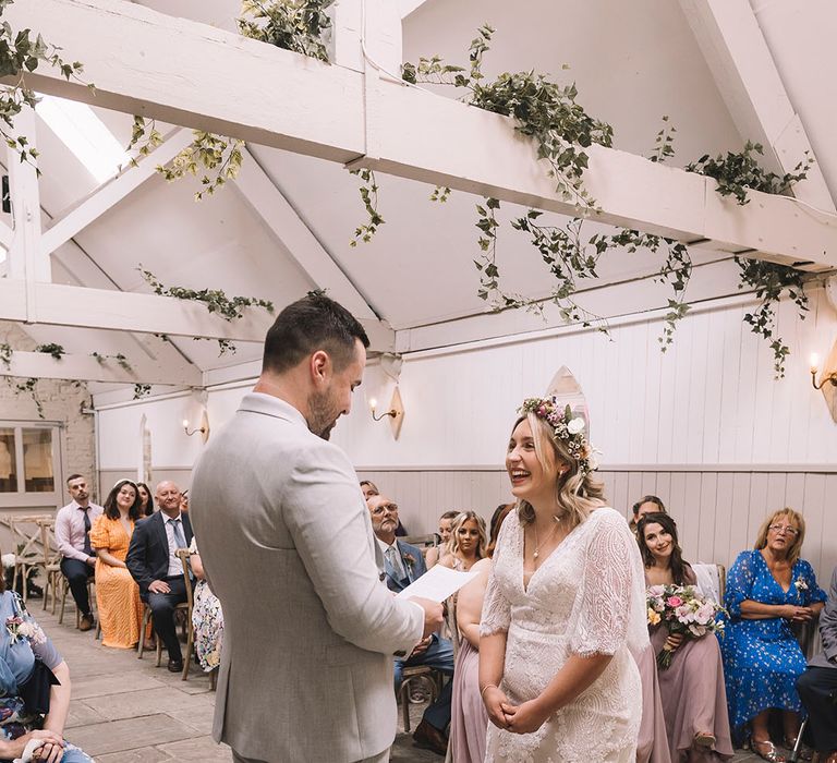 Bride in boho lace wedding dress with the groom in three piece light grey suit holding hands for their ceremony 