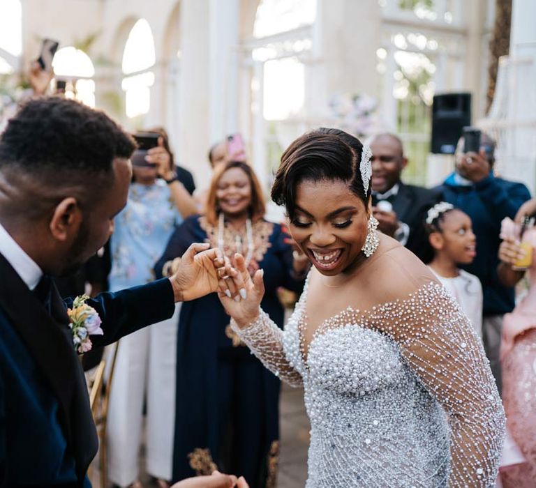 Bride in illusion v-neck sheer off shoulder long sleeve pearl embellished wedding gown dancing with groom in velvet midnight blue double breasted groom’s blazer, velvet bowtie and peach garden rose boutonniere at Syon Park vow renewal