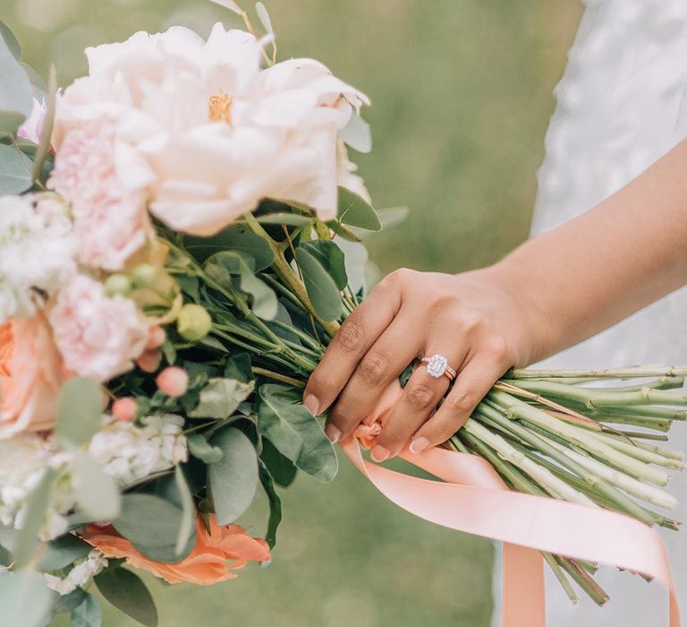 Bride holding pastel and neutral wedding bouquet with pretty diamond engagement ring and wedding band 