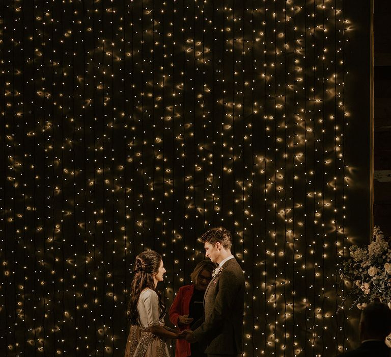 The bride and groom stand together under cosy magical lighting for multicultural ceremony 