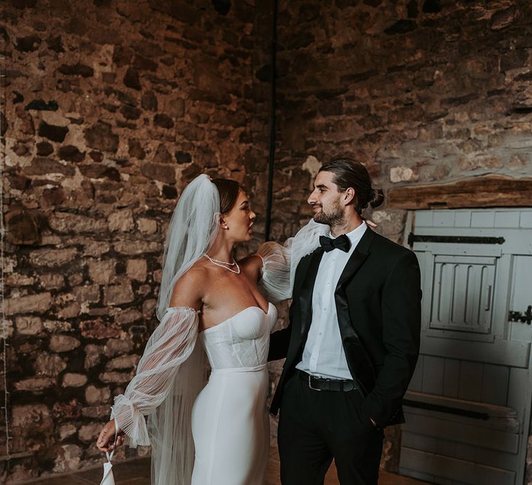 Bride wearing white wedding dress and veil standing with the groom in a black tuxedo for classic wedding at Eden Barn