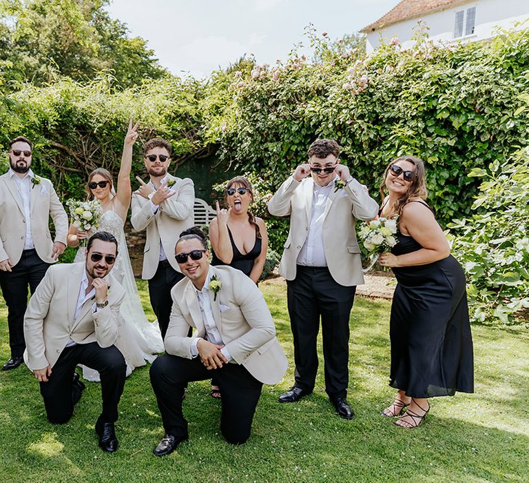 Wedding party with the groom and groomsmen in beige suits, bridesmaids in black satin bridesmaid dresses and bride in lace gown 