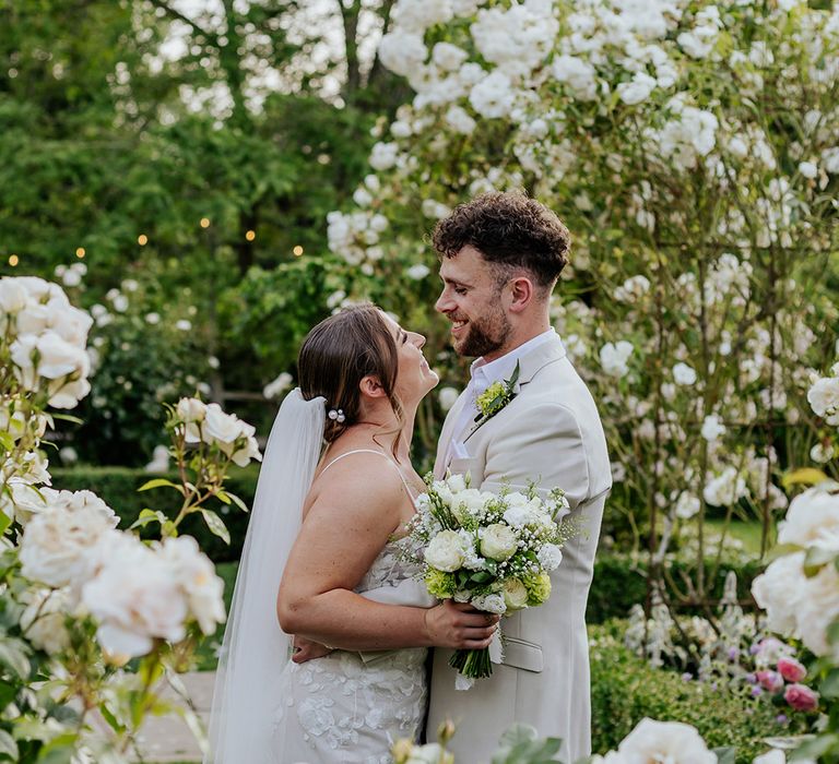 Bride and groom pose for cute couple portrait in front of white wedding flowers at Houchins 