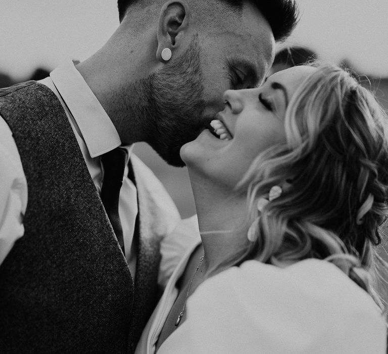 Groom in grey waistcoat kisses the bride on the head for modern wedding 