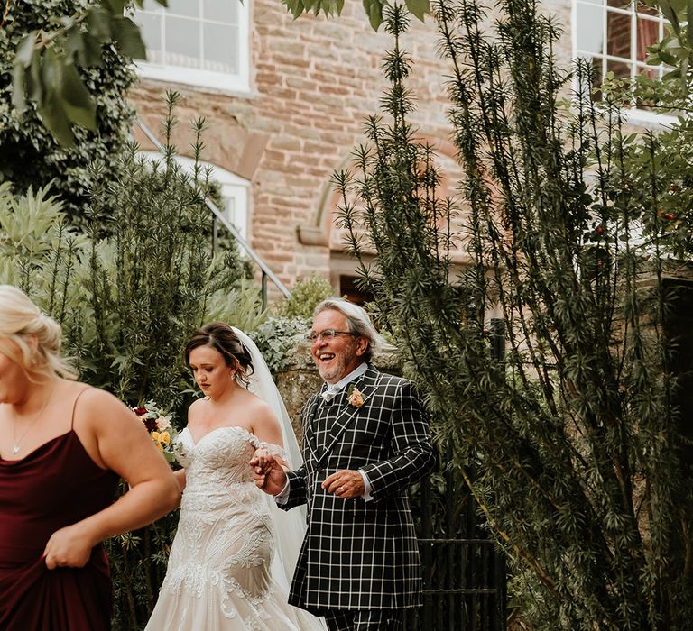 Father of the bride in checkered suit walking the bride to the church for the wedding ceremony 