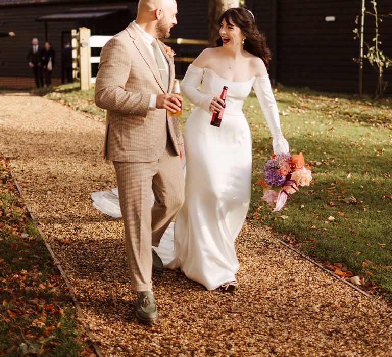 Bride in off the shoulder bespoke wedding dress walking with the groom in a checkered suit 