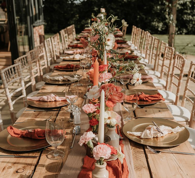 Burnt orange rustic outdoor wedding tablescape with orange table runner, with pink, peach and white wedding flowers in bud vases 