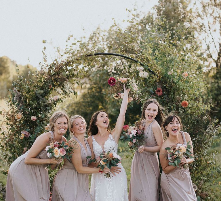 Bridesmaids in dusky pink dresses and bride in lace dress posing in front of the floral moon gate 