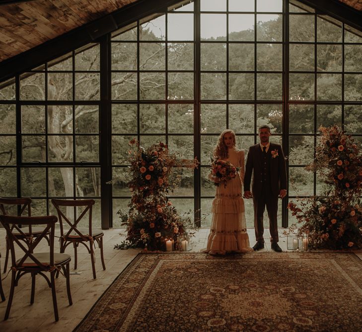 Bride and groom standing at the altar with autumn wedding flowers and wool rug 