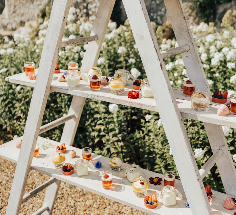 Wooden laddered shelves of picnic mini desserts with summer berries, edible flowers and chocolate covered strawberries