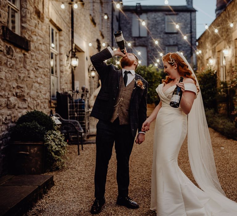 Bride and groom drinking champagne in Holmes Mill's Courtyard covered in festoon lights. 