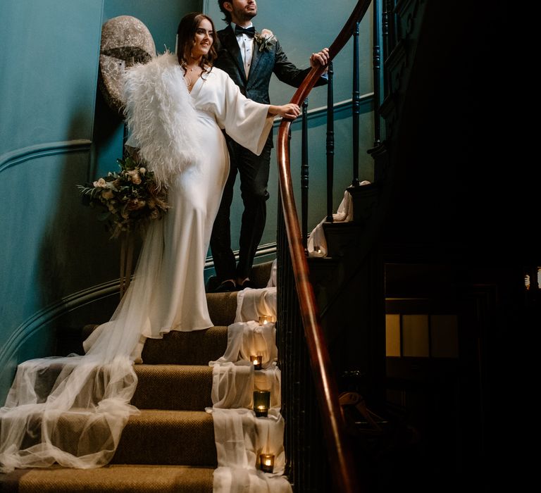 Bride and groom wedding day photography stood on stairway bride wears Marabou Fur stoleand silk wedding dress groom wears Dolce & Gabanna suit