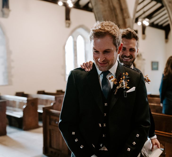 Groom wearing a kilt waits nervously at the altar