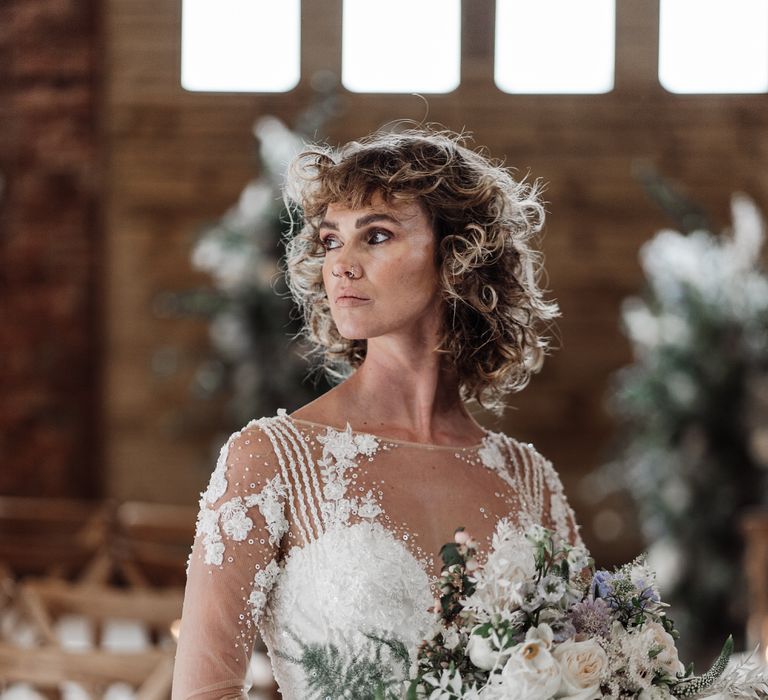 The bride with short curly wedding hair holds her bouquet of flowers and ferns