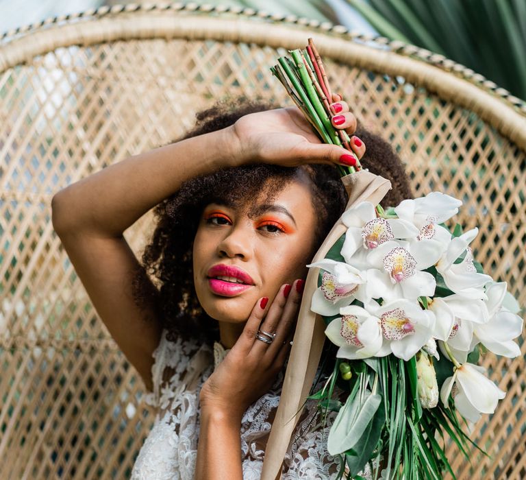 Bride with orange eyeshadow and pink lip holds jungle themed bouquet