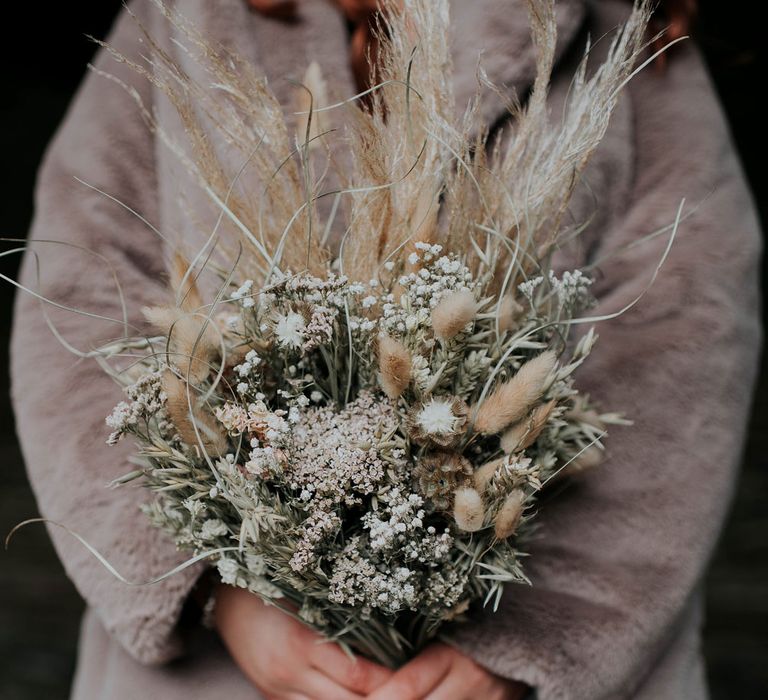 Bride in fur coat holds artisan dried flower bouquet 