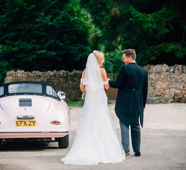 Bride and groom walking away from the camera stood next to a pink porsche in the countryside