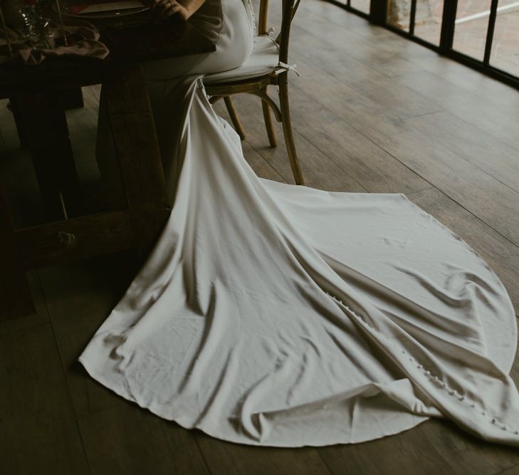 Brides train sweeps across the floor as she sits