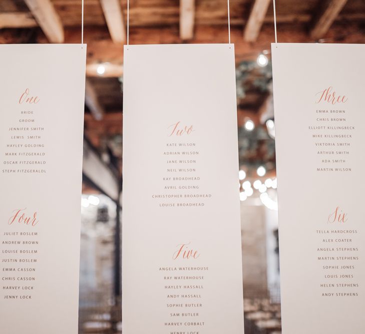 Hanging seating chart with gold font table names 