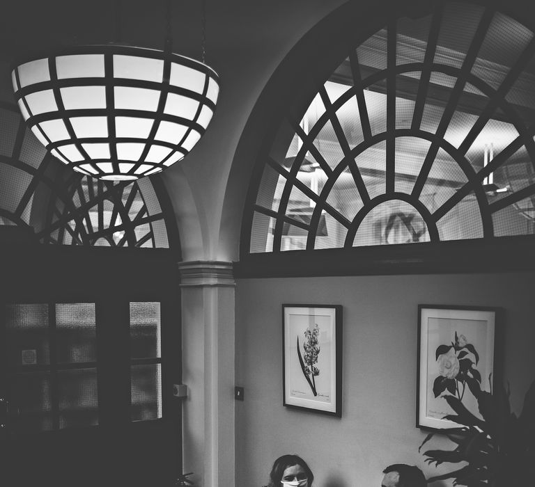 Bride & groom wears masks in black & white image as they sit within Chelsea Old Town Hall