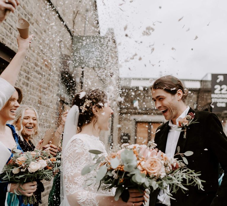 Bride and groom confetti moment with peach roses and lace long sleeved wedding dress